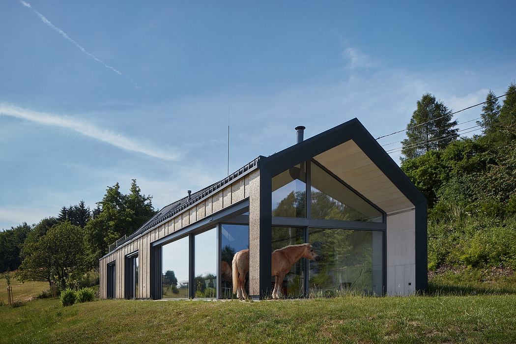 Sleek glass-walled building with a pitched roof, surrounded by greenery