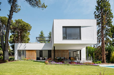 Contemporary white house with large windows, surrounded by greenery.