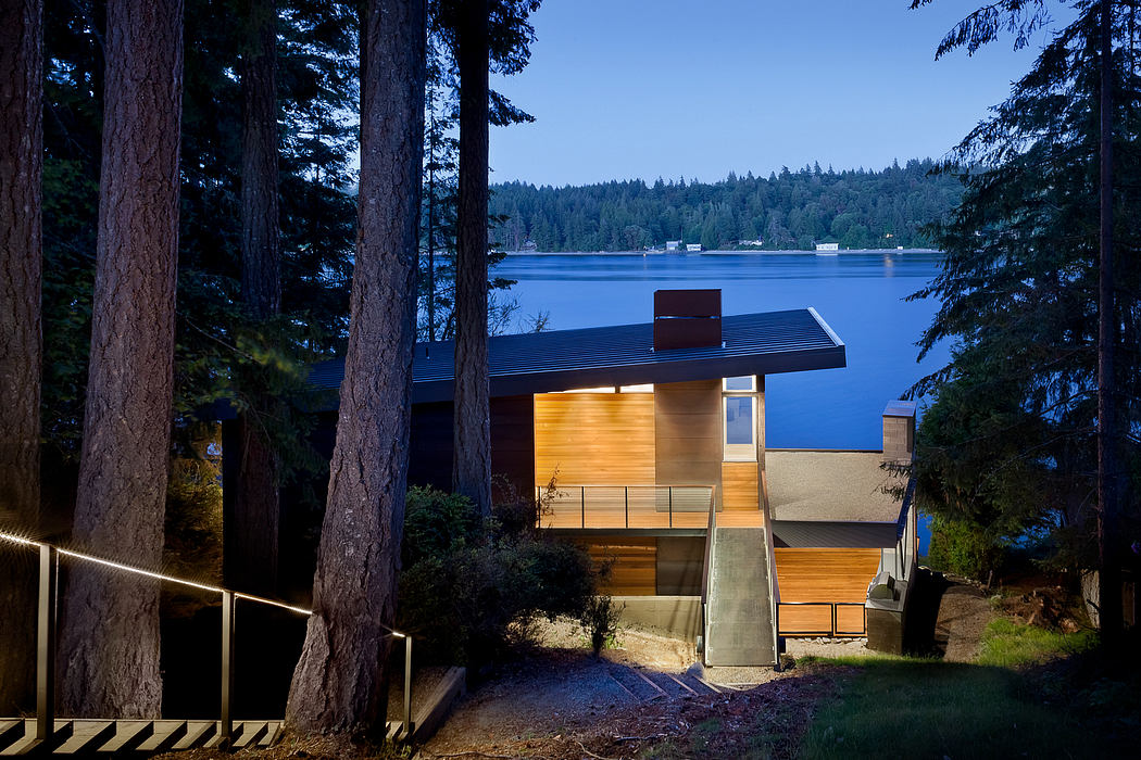 Sleek house nestled among trees with a view of a lake at dusk.
