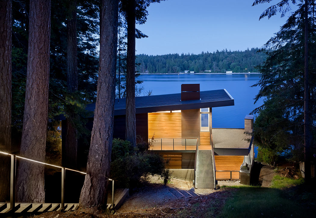 Sleek house nestled among trees with a view of a lake at dusk.