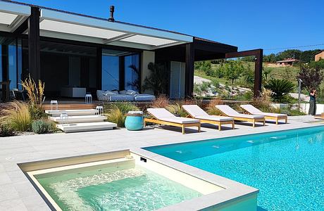 Modern house with poolside loungers and a hot tub.