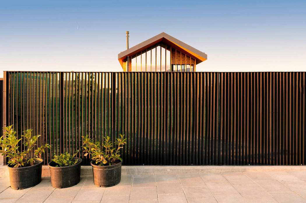 Modern house with wooden features behind a metal slat fence at dusk.