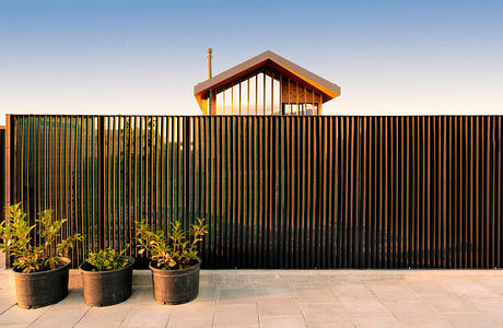 Modern house with wooden features behind a metal slat fence at dusk.