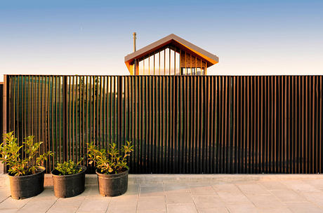 Modern house with wooden features behind a metal slat fence at dusk.