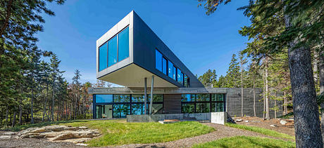 Cantilevered house with expansive glass windows amidst forest.