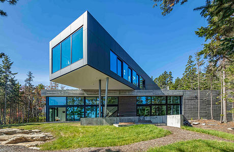 Cantilevered house with expansive glass windows amidst forest.