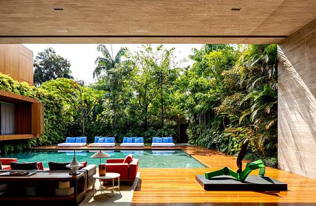 Modern living room opening onto a pool with lush greenery in the background.