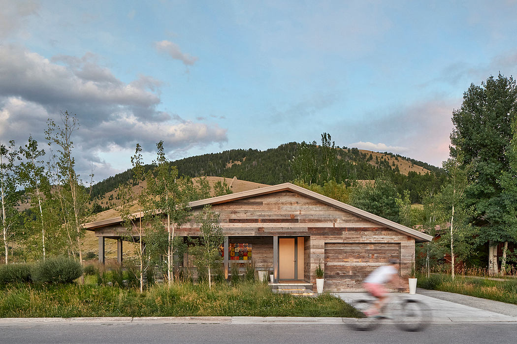 Modern wooden house with large windows against a hill, blurred cyclist in foreground.