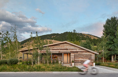 Modern wooden house with large windows against a hill, blurred cyclist in foreground.