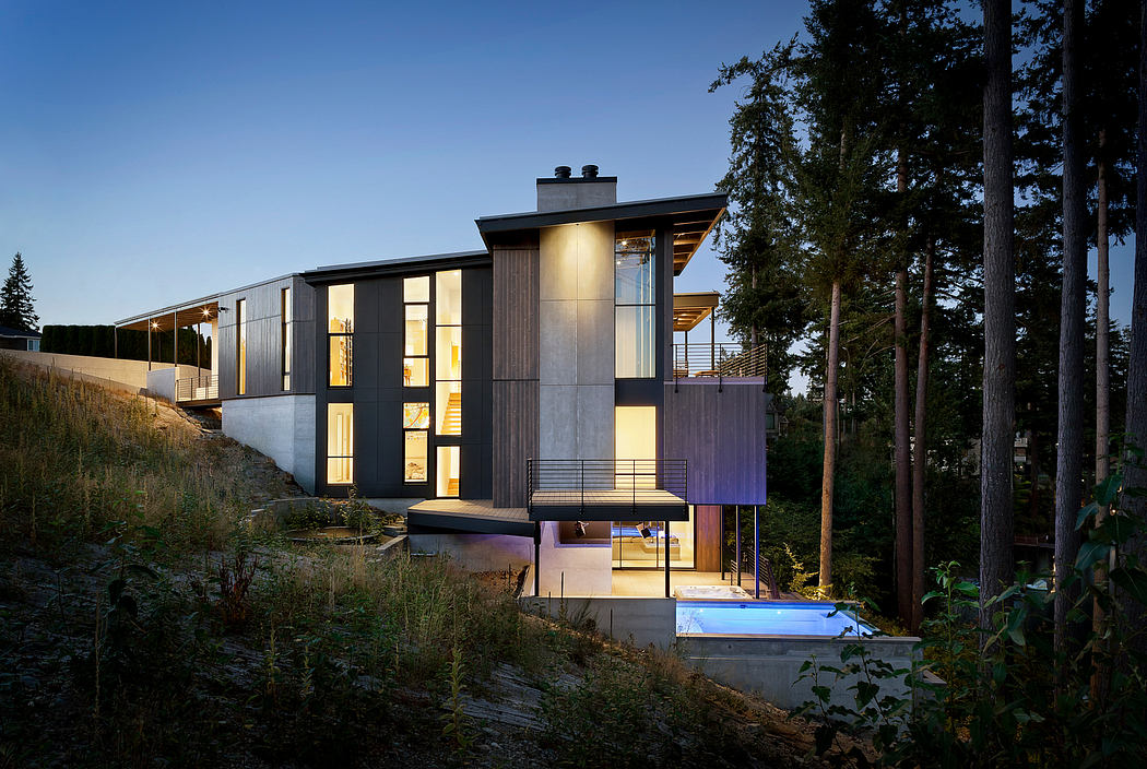 Modern house with illuminated windows at twilight, surrounded by trees.