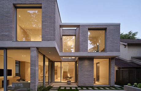 Modern two-story house with large windows illuminated at dusk.