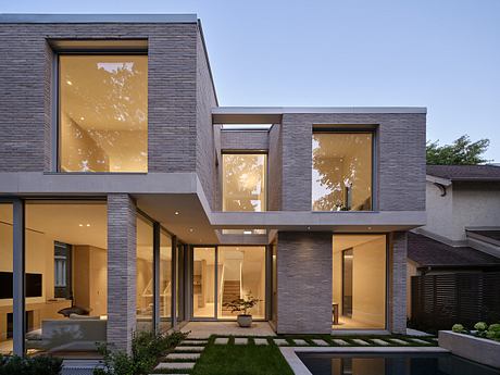 Modern two-story house with large windows illuminated at dusk.