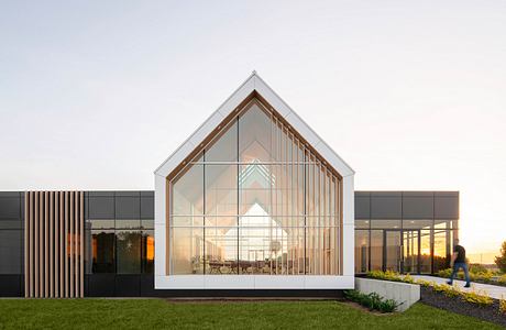 Contemporary glass-fronted gabled building at dusk with a person walking by.