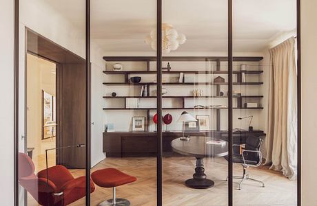 Modern living room with glass partition, elegant furniture, and shelving.