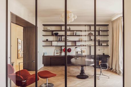 Modern living room with glass partition, elegant furniture, and shelving.