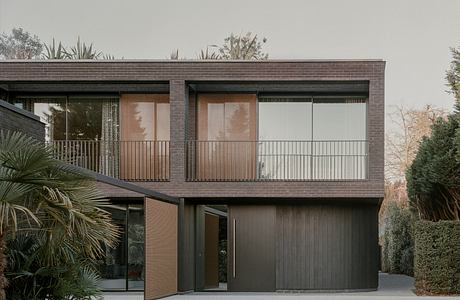 Modern two-story house with dark wood facade and glass balconies surrounded by greenery