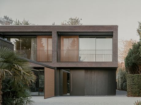 Modern two-story house with dark wood facade and glass balconies surrounded by greenery