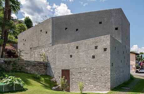 Minimalist concrete building with small windows, set in a green landscape.