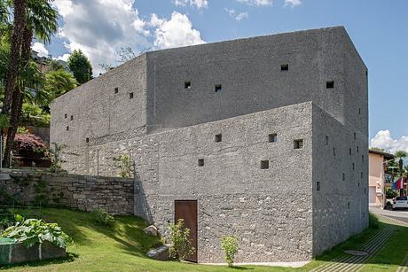 Minimalist concrete building with small windows, set in a green landscape.