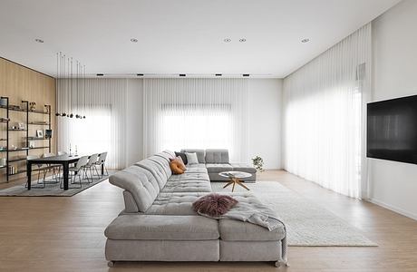 Modern minimalist living room with gray sectional sofa, wooden floors, and sheer curtains.