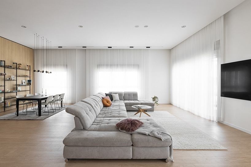 Modern minimalist living room with gray sectional sofa, wooden floors, and sheer curtains.