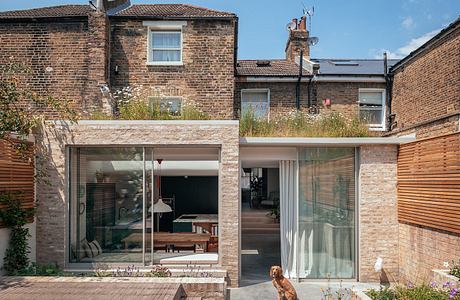 Contemporary brick extension with large glass windows and a dog sitting outside.