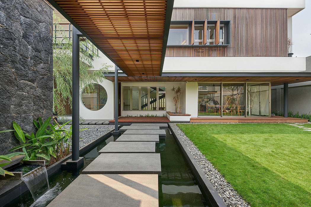 Contemporary house with wooden overhang, stone path over water, and lush lawn