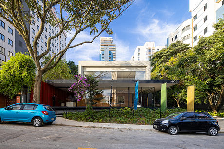 Modern commercial storefront with glass facade and colorful accents, flanked by trees and parked