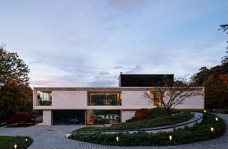 Contemporary house with large windows amid landscaped garden at dusk.