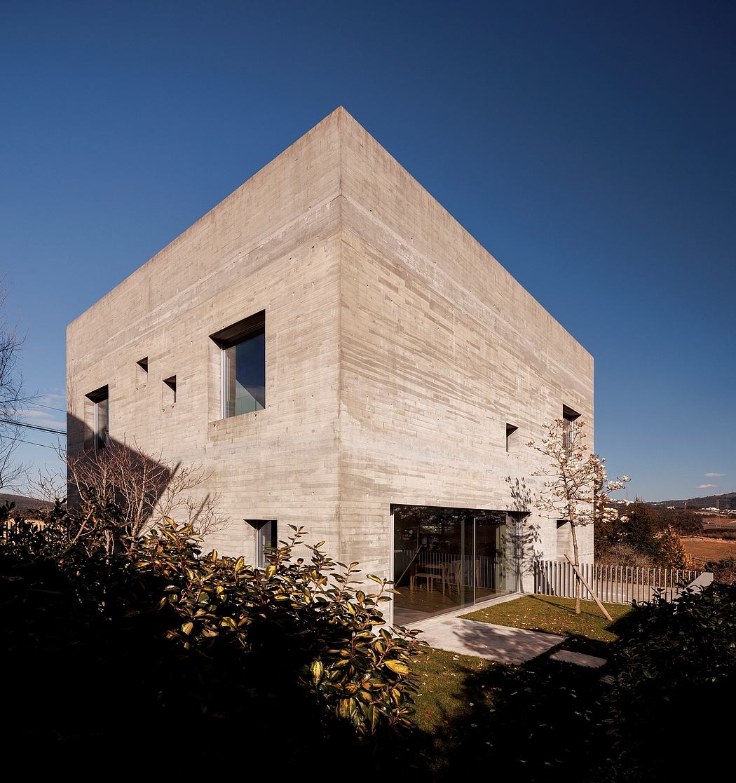 Cuboid concrete building with asymmetrical windows under a clear sky.