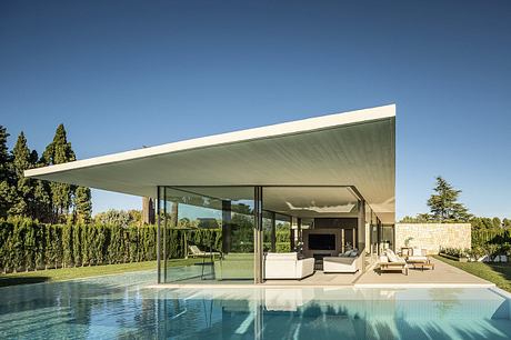 Modern house with large glass walls and flat roof overlooking a pool.