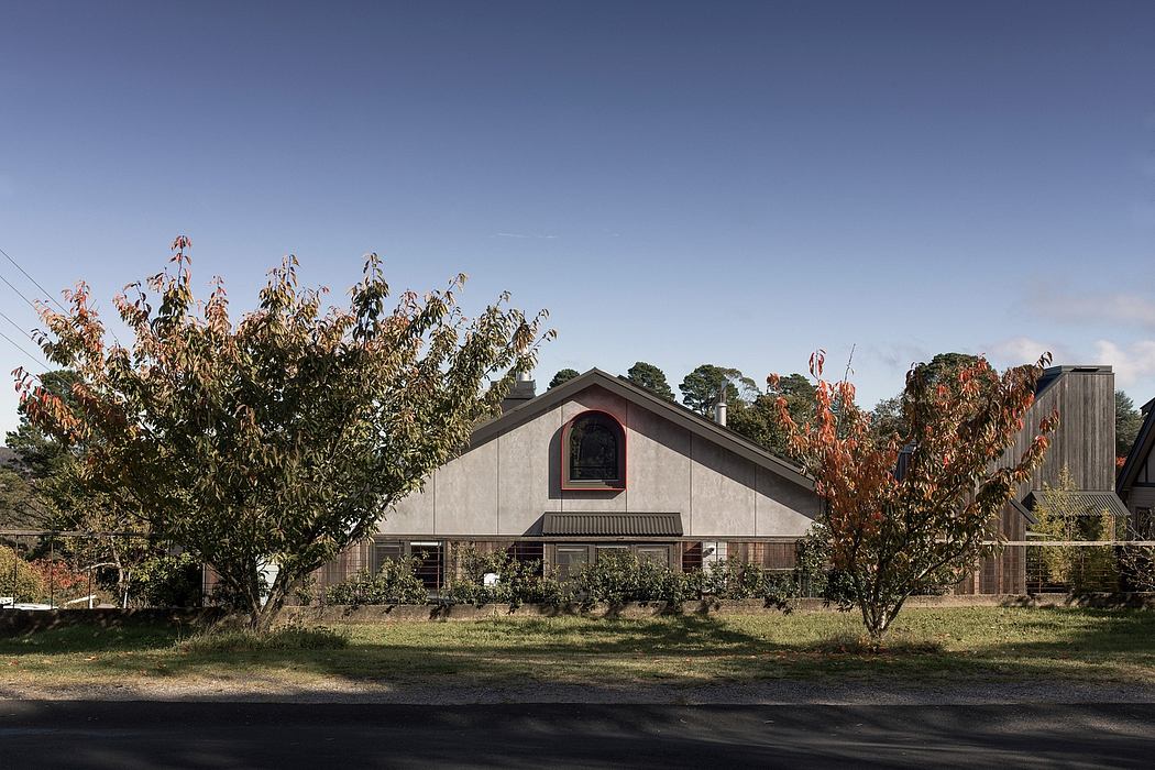 A barn-style house with a prominent arched window, surrounded by autumn trees.