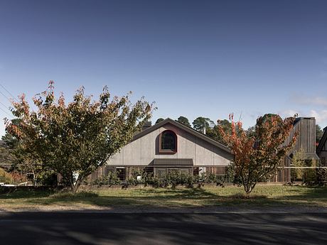 A barn-style house with a prominent arched window, surrounded by autumn trees.