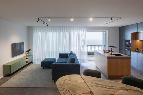 Modern living room with ocean view, blue sofa, and open kitchen.