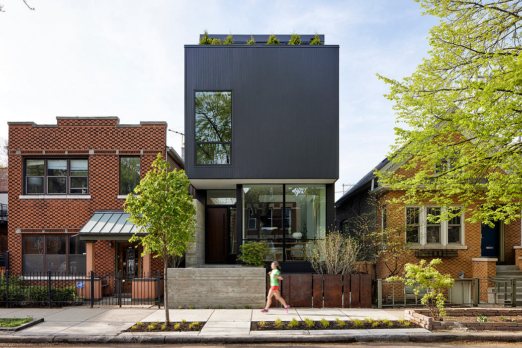 Modern three-story black residential building sandwiched between traditional brick houses.