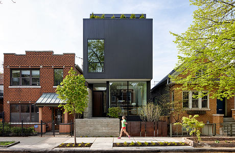 Modern three-story black residential building sandwiched between traditional brick houses.