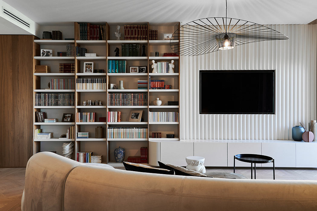 Contemporary living room with expansive bookshelf, TV, and artistic light fixture.