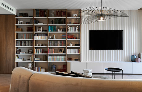 Contemporary living room with expansive bookshelf, TV, and artistic light fixture.