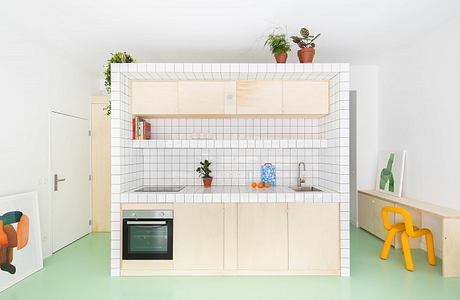 Minimalist kitchen with light wood cabinets and green floor.