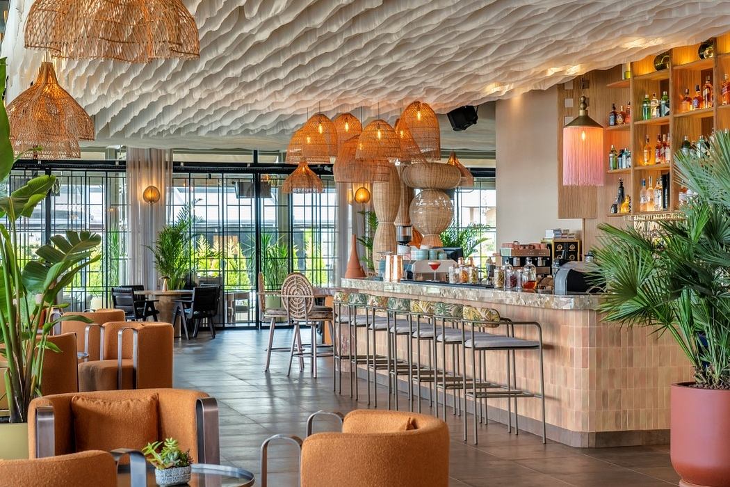 Modern cafe interior with wavy ceiling design and hanging wicker lamps.