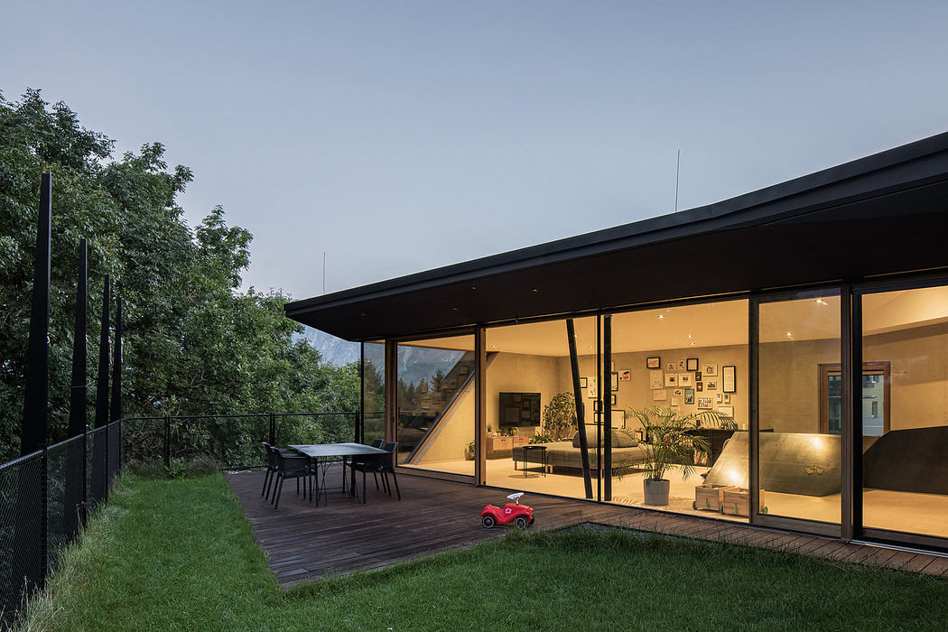 Modern house with large glass windows and outdoor dining area at dusk.