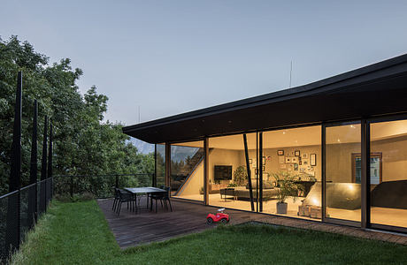 Modern house with large glass windows and outdoor dining area at dusk.