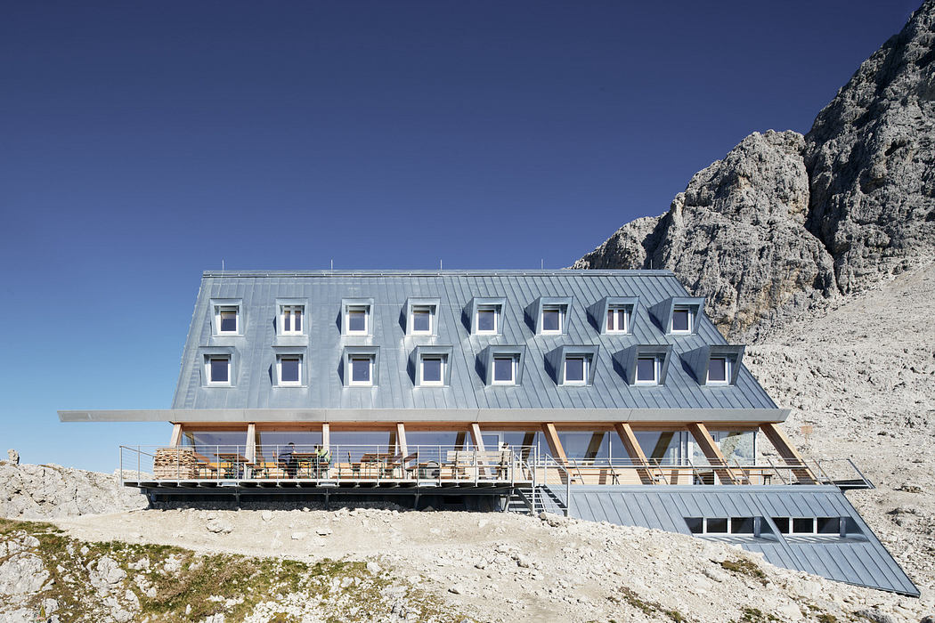 Modern mountain lodge with geometric facade against a rocky backdrop.