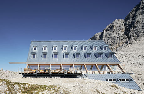 Modern mountain lodge with geometric facade against a rocky backdrop.