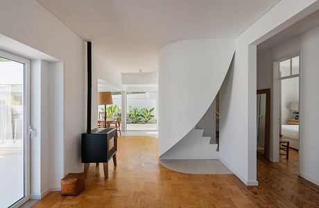 Modern interior with curved staircase, wooden flooring, and minimalistic furniture.