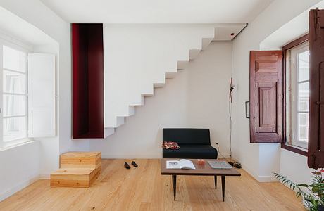 Minimalist living room with a white staircase, wooden floor, and black sofa.