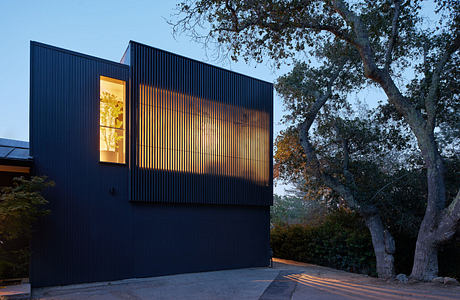 Contemporary dark-hued building with illuminated slatted facade at dusk.