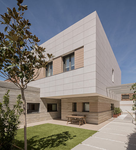 Modern cubic house with beige exterior, wooden accents, and a small garden.