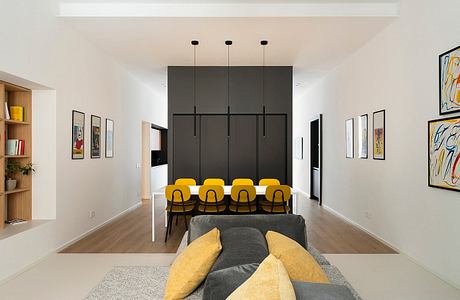 Modern dining room with yellow chairs, art on walls, and black cupboard.