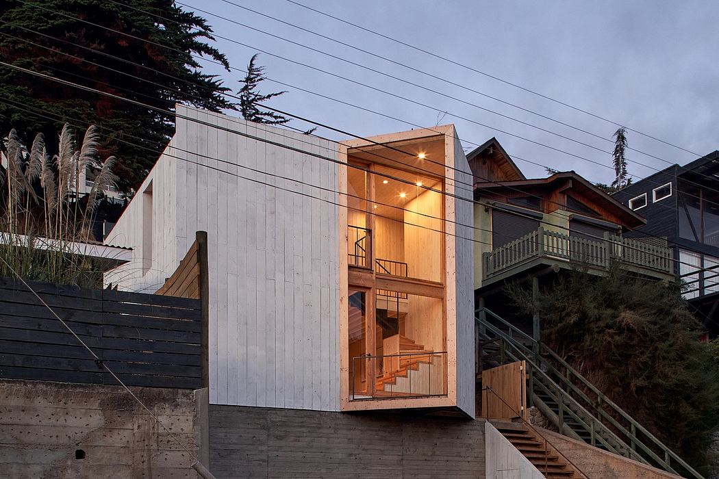 Modern beach house with illuminated interior at dusk, concrete stairs on the side.